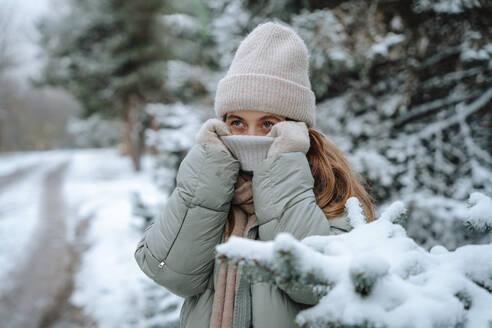 Verspielte Frau bedeckt Gesicht mit Pullover im Winter - NLAF00250