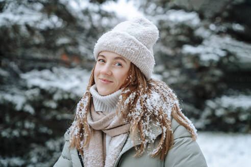 Lächelnde Frau mit Strickmütze auf Schnee im Winter - NLAF00253