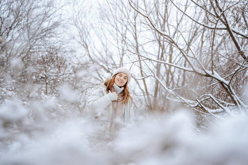 Glückliche Frau inmitten von gefrorenen Bäumen auf Schnee im Winter - NLAF00264