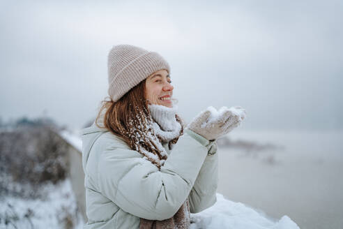 Happy woman holding snow in cupped hands - NLAF00271
