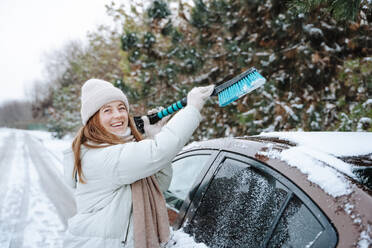Glückliche Frau, die im Winter Schnee vom Auto entfernt - NLAF00274