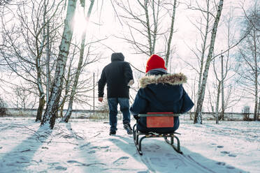 Vater zieht Sohn auf Schlitten sitzend im Winter - NLAF00280