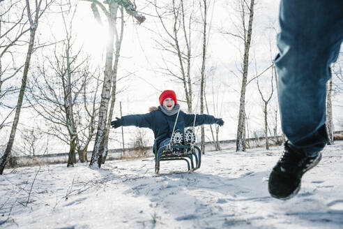 Cheerful son enjoying sled ride on snow in winter - NLAF00281