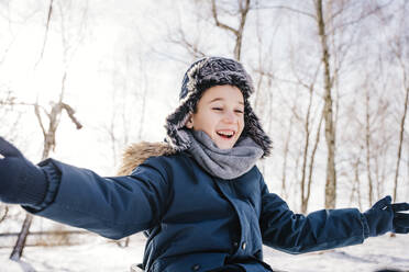 Fröhlicher Junge mit ausgestreckten Armen, der im Winter Spaß hat - NLAF00285