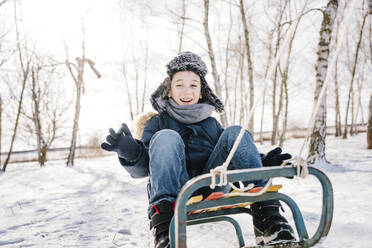 Glücklicher Junge beim Schlittenfahren auf Schnee im Winter - NLAF00286