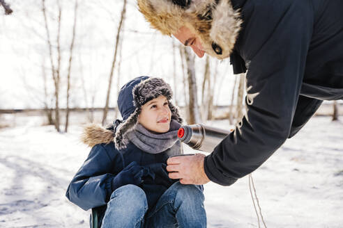 Vater serviert seinem Sohn im Winter heißen Tee im Schnee - NLAF00287