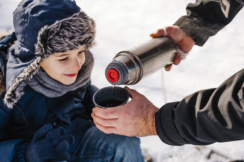 Father pouring hot tea in cup for son in winter - NLAF00288