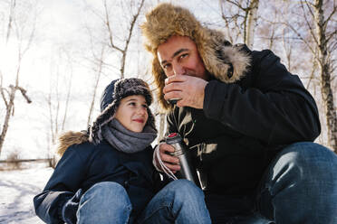 Father drinking tea sitting next to son in winter - NLAF00289