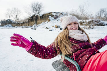 Fröhliches Mädchen genießt Schlittenfahrt auf Schnee im Winter - NLAF00298