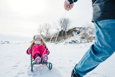 Vater fährt Tochter auf Schlitten sitzend im Winter - NLAF00299