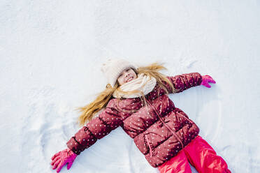 Carefree girl lying down on snow in winter - NLAF00300