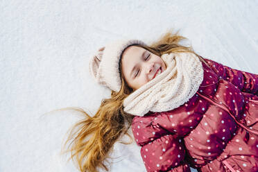 Glückliches blondes Mädchen liegt mit geschlossenen Augen im Schnee - NLAF00301