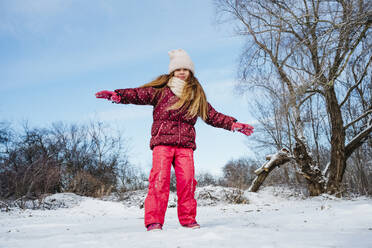 Glückliches Mädchen steht mit ausgestreckten Armen im Schnee im Winter - NLAF00303