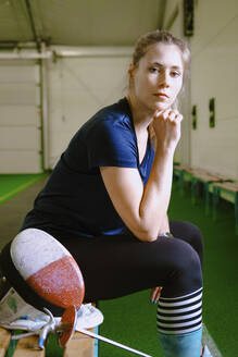 Confident woman with hand on chin sitting on bench in gym - YHF00105