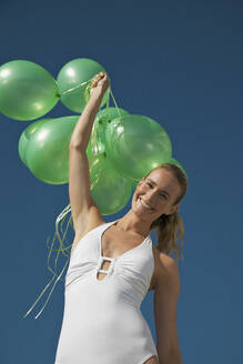 Frau hält ein Bündel grüner Luftballons und lächelt - Tiefblick - FSIF06810