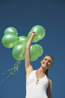 Frau hält ein Bündel grüner Luftballons und lächelt - Tiefblick - FSIF06811