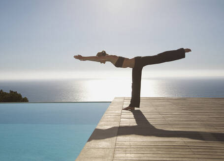 Junge Frau übt Yoga an einem Swimmingpool mit dem Meer im Hintergrund - FSIF06820