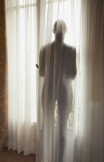 Silhouette einer Frau hinter einem halbtransparenten Vorhang, Rückenansicht - FSIF06824