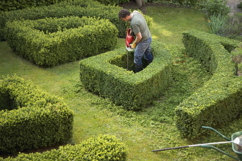 Gärtner schneidet eine Hecke in einem Labyrinth mit einer elektrischen Schere, Blick von oben - FSIF06827