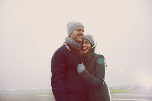 Lächelndes Paar, das sich auf der Startbahn des Flughafens umarmt - FSIF06845