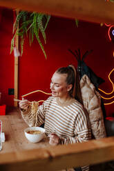 Smiling woman eating ramen at restaurant - MDOF01820