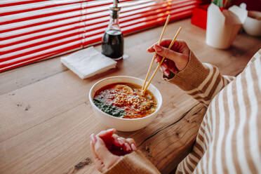 Woman eating ramen noodles using chopsticks at restaurant - MDOF01826