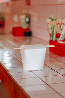 Chinesischer Takeout-Behälter mit Stäbchen auf dem Tisch im Restaurant - MDOF01831