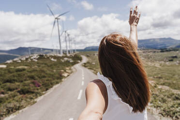 Spain, Madrid, Back of woman reaching toward clouds in front of wind farm - EBBF08601