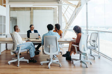 Business people collaborating in a modern office. They are engaged in a brainstorming session, discussing ideas and planning a project. The team demonstrates effective teamwork and emphasizes diversity and inclusion in the workplace. - JLPSF31136