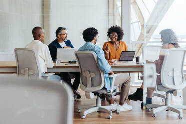 Eine Gruppe von Geschäftsleuten in einer lebhaften Diskussion und Brainstorming-Sitzung. Sie arbeiten zusammen, tauschen Ideen aus und lächeln begeistert. Dieses dynamische Team ist ein Beispiel für erfolgreiche Teamarbeit an einem modernen, produktiven Arbeitsplatz. - JLPSF31139