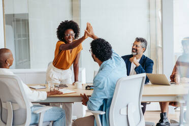 Fachleute feiern ihre Leistungen mit einem High Five und fördern so die Teamarbeit und den Erfolg in diesem kreativen Startup-Umfeld. Geschäftsleute arbeiten in einer lebhaften Büroumgebung zusammen. - JLPSF31143