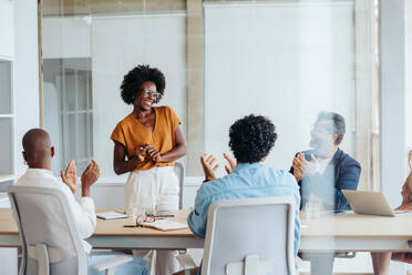 Business professionals discussing a project in a boardroom. They collaborate and celebrate their successful teamwork. Happy colleagues applauding, showcasing creativity and dedication in a vibrant workplace. - JLPSF31146