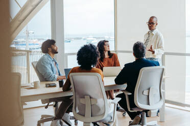 Diverse business professionals collaborating at an office table, brainstorming and discussing ideas for a project. They demonstrate teamwork and focus during this business meeting. - JLPSF31152