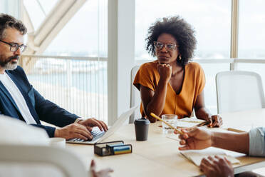 Eine Gruppe von Geschäftsleuten in einem modernen Büro führt eine kreative und kollaborative Diskussion, an der sich die schwarze Frau aktiv beteiligt und ihre unternehmerischen Fähigkeiten unter Beweis stellt. - JLPSF31158