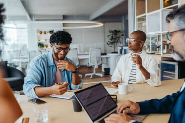 Young business people brainstorming ideas for a project. They use laptops and discuss business plans. The atmosphere is positive and collaborative, with happy colleagues working together as a team. - JLPSF31172