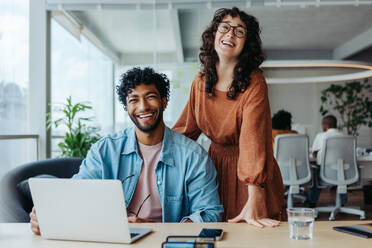 Two business people working on creative projects in a modern office. Focused on work, they demonstrate successful teamwork. Smiling and confident, this dynamic team strives for success in their startup. - JLPSF31183