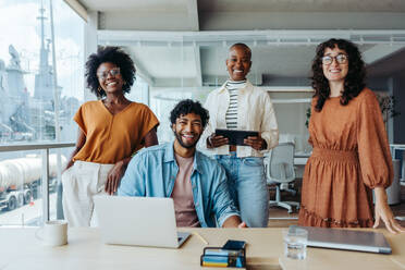 Multicultural group of professionals showcasing their teamwork and success in a modern office. The colleagues are dressed in business casual and looking at the camera looking happy. - JLPSF31185