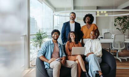 Eine Gruppe von Fachleuten in legerer Business-Kleidung arbeitet in einem modernen Büro fröhlich an einem Laptop. Ihre Teamarbeit und Professionalität tragen zu ihrem Erfolg in diesem kreativen Arbeitsbereich bei. - JLPSF31188