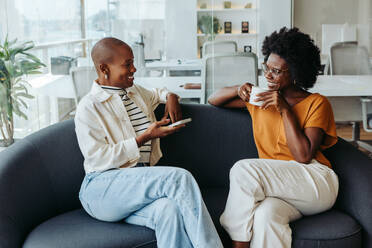 Two business women having a coffee break and chatting on a modern office sofa. They are working together in a professional team. - JLPSF31194