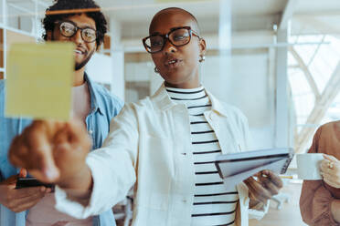 Business woman engaging in a creative brainstorming session with her team in a glass-walled office. Professionals collaborating, discussing ideas, and demonstrating teamwork in a startup. - JLPSF31199