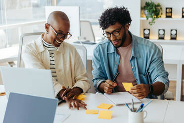 Business people engage in a lively discussion, brainstorming ideas for a project. Sticky notes with various concepts and notes are scattered on the table. The team members exhibit a sense of cooperation and teamwork, creating a productive and creative workplace environment. - JLPSF31219