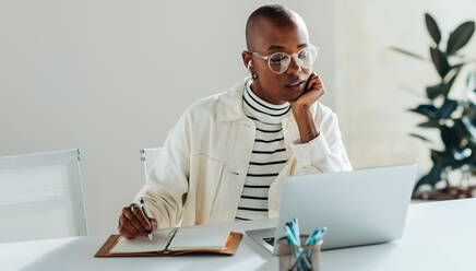 Woman using laptop in a bright office space, portraying concepts of professionalism, concentration, and modern work environment. She exudes confidence and determination with a touch of creative thinking. - JLPSF31282