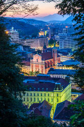 Die Dämmerung bricht über Ljubljana herein und lässt die roten und gelben Fassaden der historischen Gebäude vor der Kulisse der Berge und des dämmrigen Himmels aufleuchten - ADSF52774
