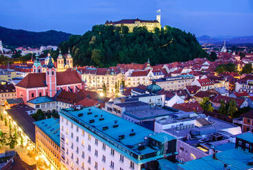 Night falls on Ljubljana with a view of the castle overlooking the city's glowing historical architecture and streets - ADSF52776