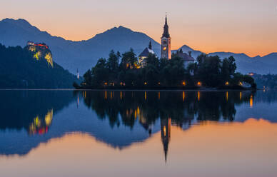 The sun sets on Lake Bled, casting a warm glow on the Pilgrimage Church of the Assumption of Maria and the Bled Castle - ADSF52779