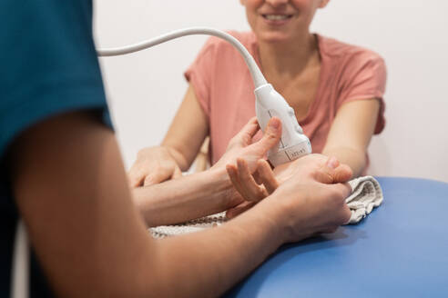 Eine lächelnde Patientin, die sich einer Ultraschalltherapie zur Behandlung ihrer Hände unterzieht, begleitet von einer medizinischen Fachkraft - ADSF52836