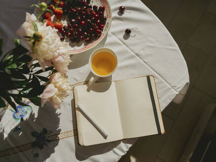 Open diary near teacup and cherries on table at home - IEF00528