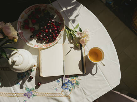 Diary near teapot and fruits on table at home - IEF00529