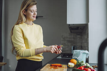 Young woman peeling vegetables in kitchen at home - OLRF00146