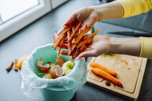 Hands of young woman putting carrot peels in garbage can at home - OLRF00148